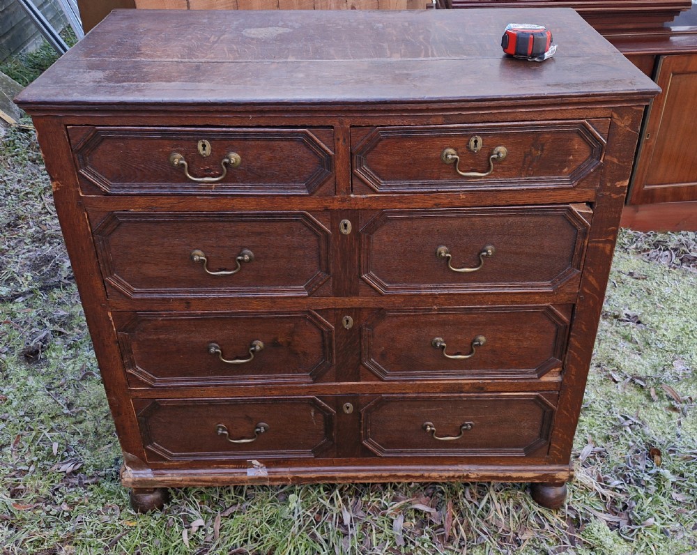 An 18th-century dark oak chest of drawers featuring geometric octagonal panel mouldings, brass drop handles, keyhole escutcheons, and turned bun feet. View XI