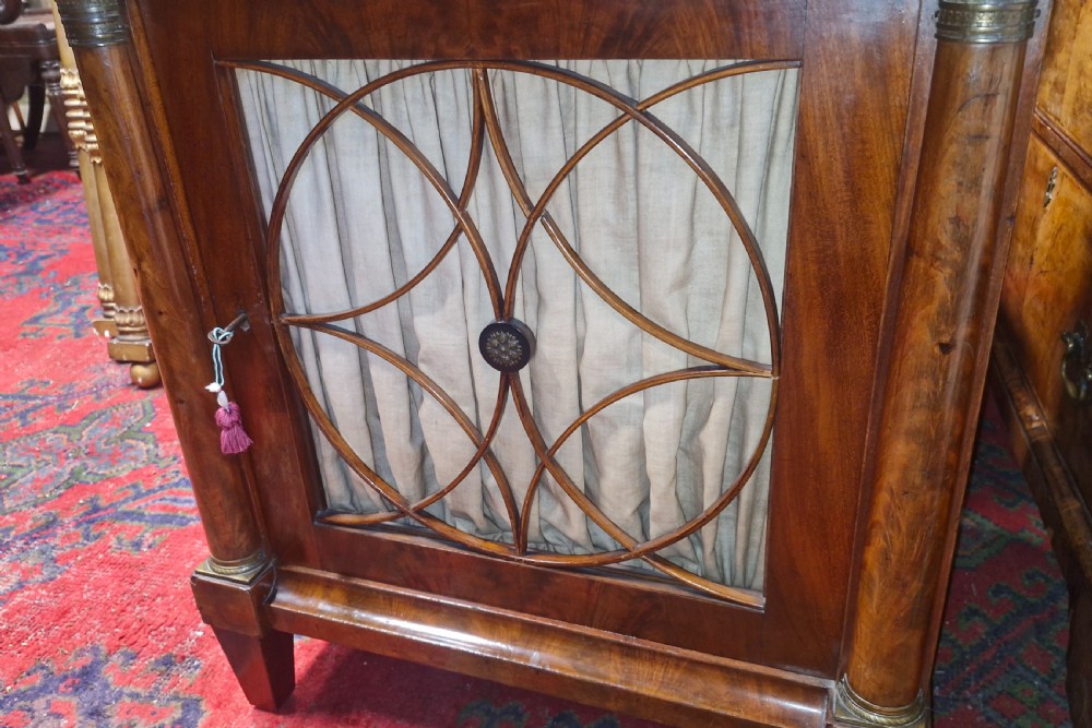 An Early Victorian mahogany single door side cabinet featuring a flame mahogany top and a decorative geometric fretwork door panel backed with fabric. View XI