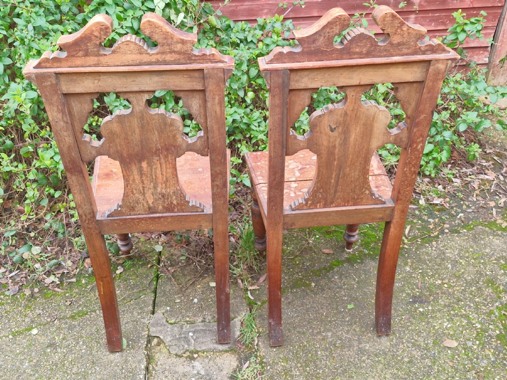 A pair of late Victorian wooden hall chairs featuring ornate carved back splats, crest pediments, solid wood seats, and turned front legs. View IV