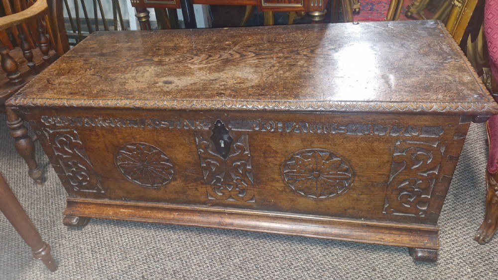 A dark brown 18th-century carved oak blanket chest featuring rosette relief carvings, a carved top frieze, and a central iron escutcheon.