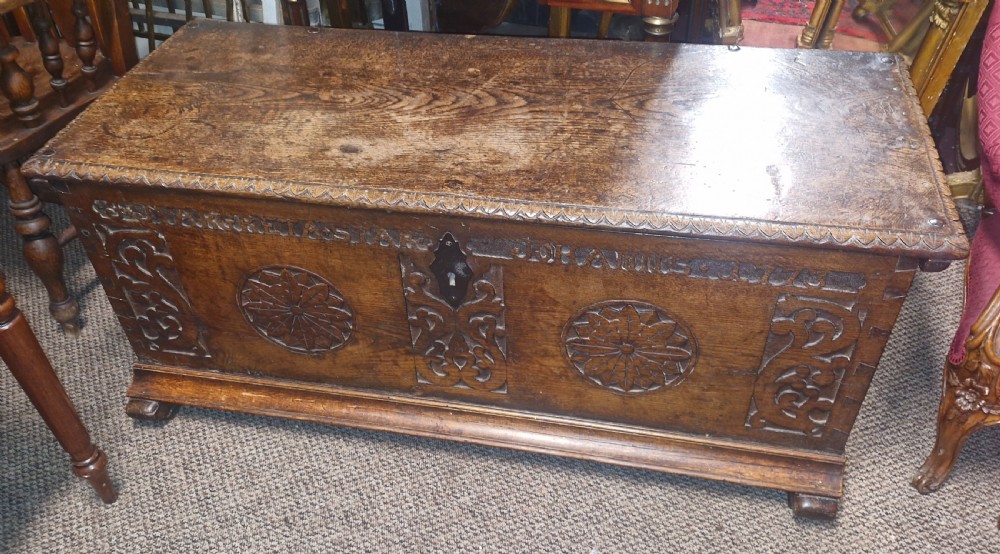 A dark brown 18th-century carved oak blanket chest featuring rosette relief carvings, a carved top frieze, and a central iron escutcheon. View II