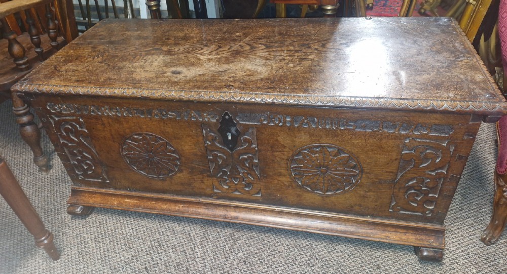A dark brown 18th-century carved oak blanket chest featuring rosette relief carvings, a carved top frieze, and a central iron escutcheon. View III