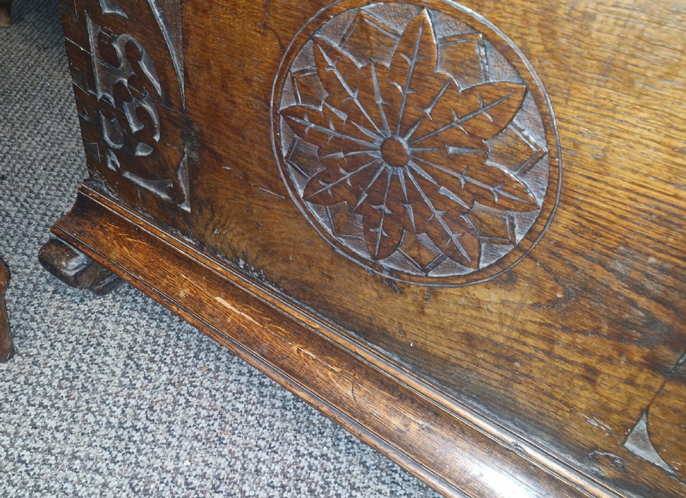 A dark brown 18th-century carved oak blanket chest featuring rosette relief carvings, a carved top frieze, and a central iron escutcheon. View VI
