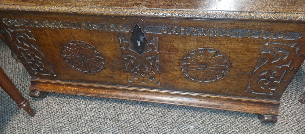 A dark brown 18th-century carved oak blanket chest featuring rosette relief carvings, a carved top frieze, and a central iron escutcheon. View VIII