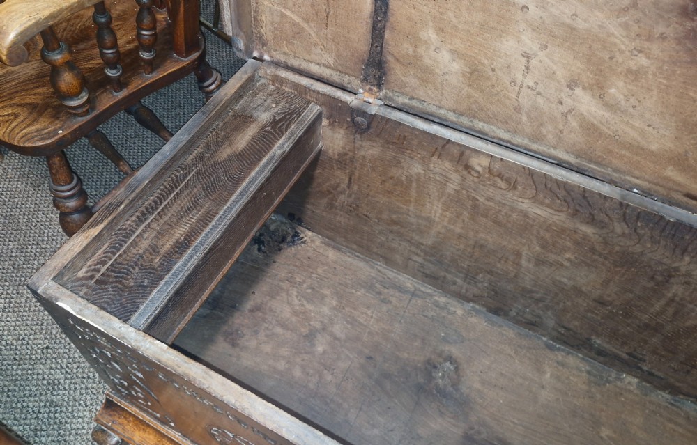 A dark brown 18th-century carved oak blanket chest featuring rosette relief carvings, a carved top frieze, and a central iron escutcheon. View IX