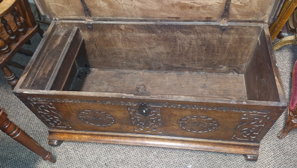 A dark brown 18th-century carved oak blanket chest featuring rosette relief carvings, a carved top frieze, and a central iron escutcheon. View X