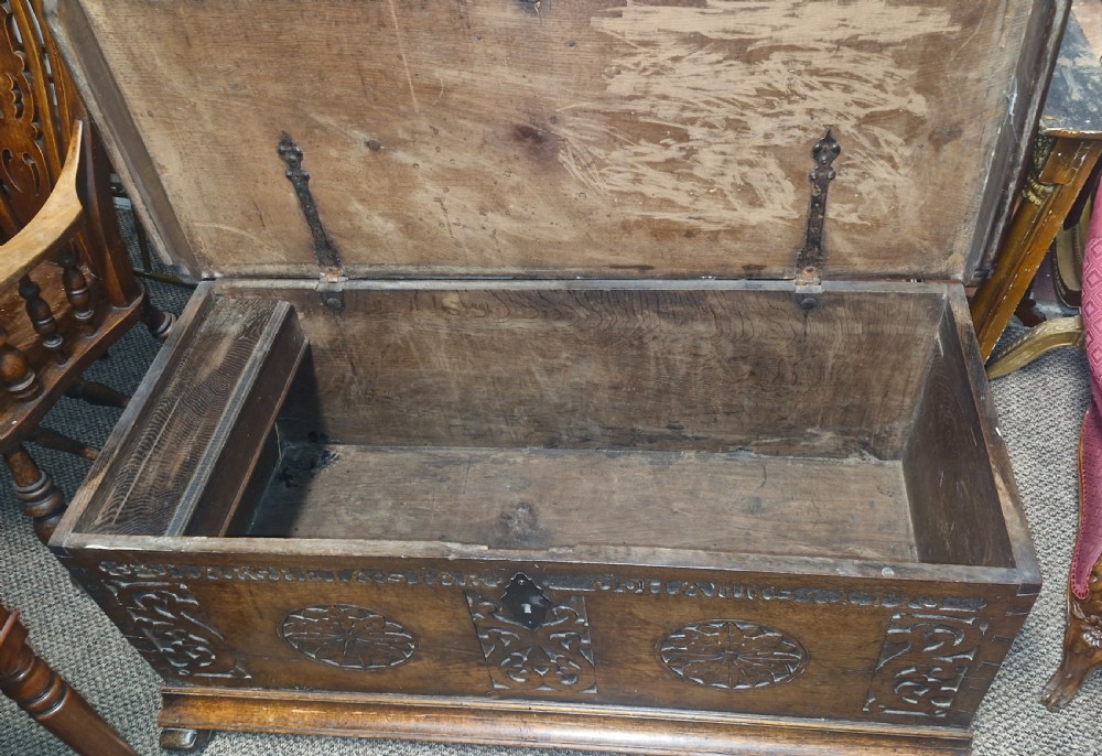 A dark brown 18th-century carved oak blanket chest featuring rosette relief carvings, a carved top frieze, and a central iron escutcheon. View XI