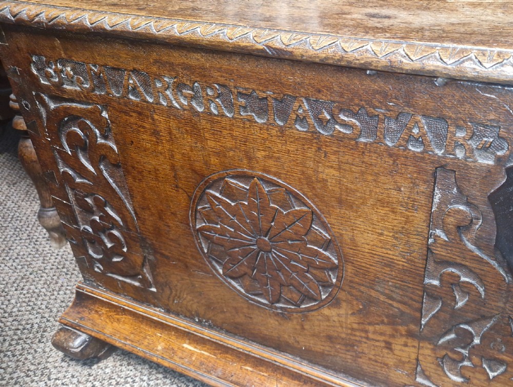 A dark brown 18th-century carved oak blanket chest featuring rosette relief carvings, a carved top frieze, and a central iron escutcheon. View XIV