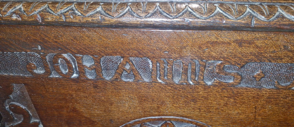 A dark brown 18th-century carved oak blanket chest featuring rosette relief carvings, a carved top frieze, and a central iron escutcheon. View XV