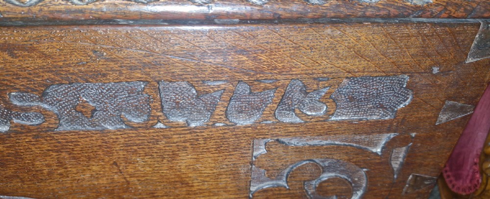 A dark brown 18th-century carved oak blanket chest featuring rosette relief carvings, a carved top frieze, and a central iron escutcheon. View XVI
