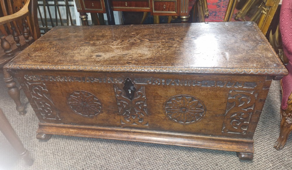 A dark brown 18th-century carved oak blanket chest featuring rosette relief carvings, a carved top frieze, and a central iron escutcheon. View XVII