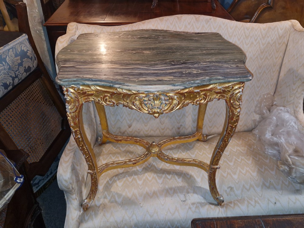 A carved giltwood occasional table featuring cabriole legs, ornate scroll carving, and a shaped veined green marble top. View IX