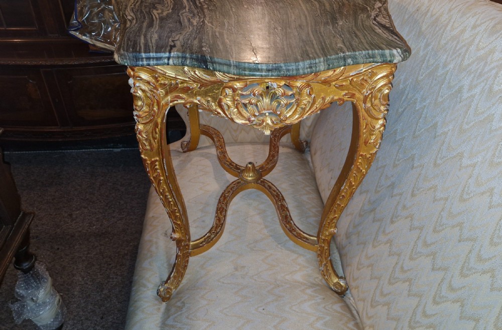 A carved giltwood occasional table featuring cabriole legs, ornate scroll carving, and a shaped veined green marble top. View X