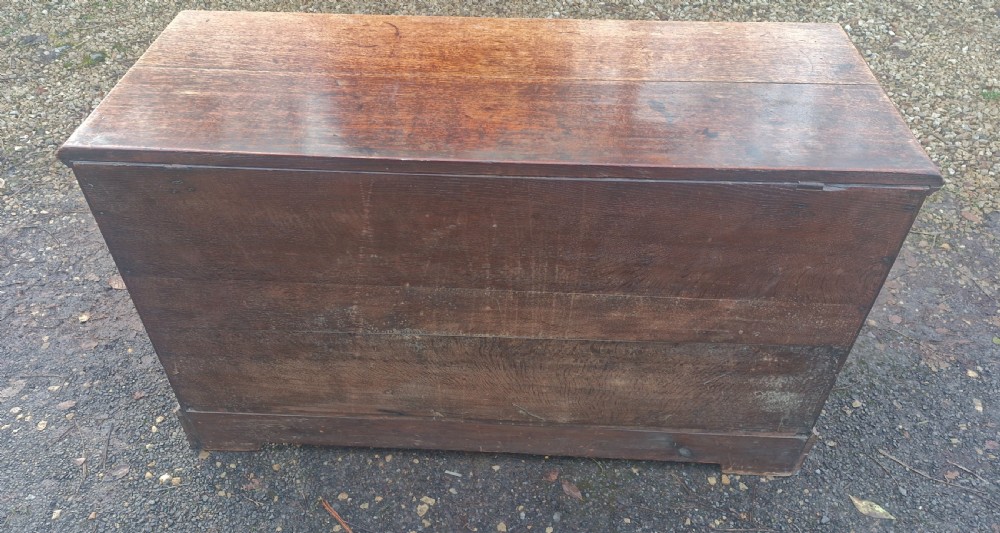 A late Georgian oak blanket chest featuring three fielded front panels, two lower drawers with brass drop handles, and a hinged lid. View II