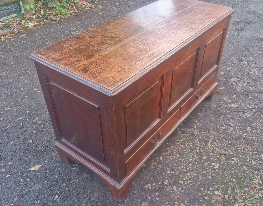 A late Georgian oak blanket chest featuring three fielded front panels, two lower drawers with brass drop handles, and a hinged lid. View III