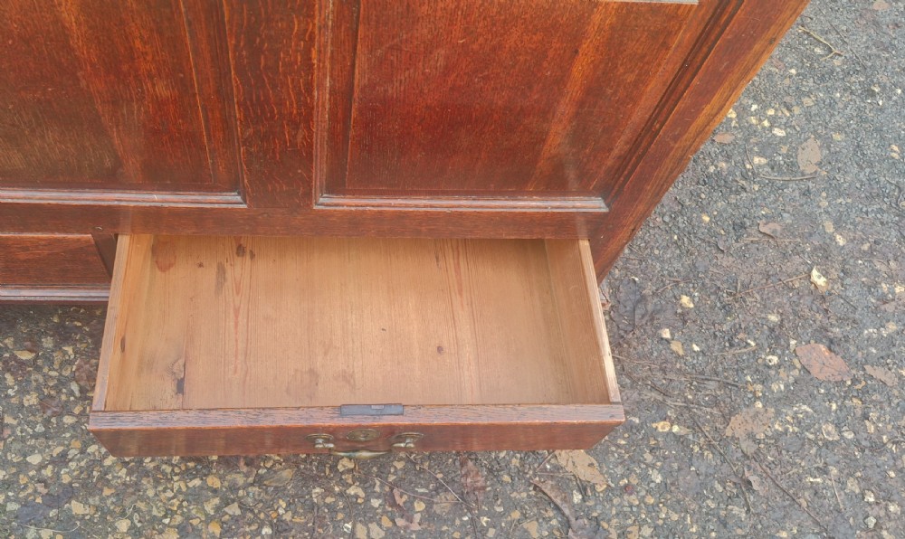 A late Georgian oak blanket chest featuring three fielded front panels, two lower drawers with brass drop handles, and a hinged lid. View IX