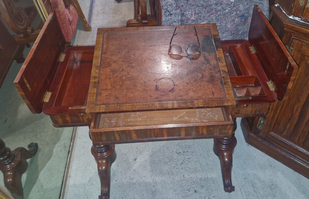 A Regency mahogany writing table featuring a central leather-inset writing surface and two hinged side flaps revealing interior storage compartments. View IX