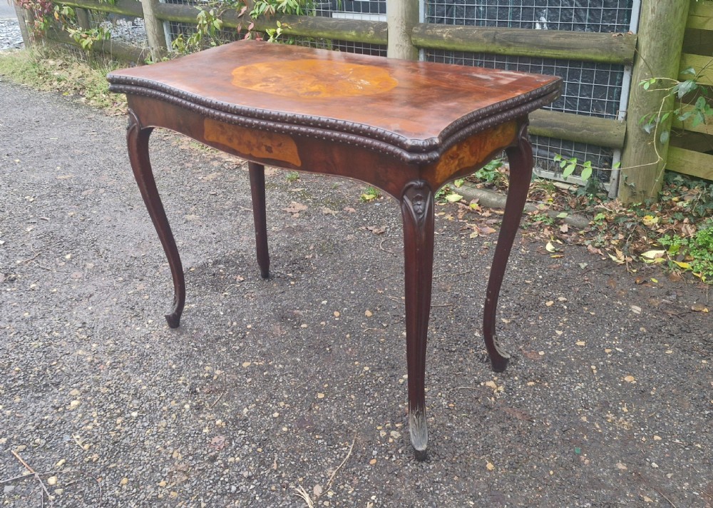 An 18th-century mahogany games table featuring a serpentine front, cabriole legs with carved knees, and marquetry inlay on the top.
