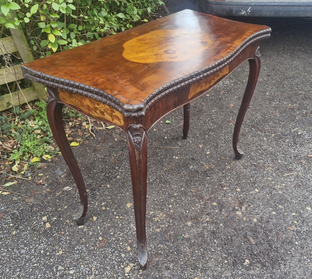 An 18th-century mahogany games table featuring a serpentine front, cabriole legs with carved knees, and marquetry inlay on the top. View XVI