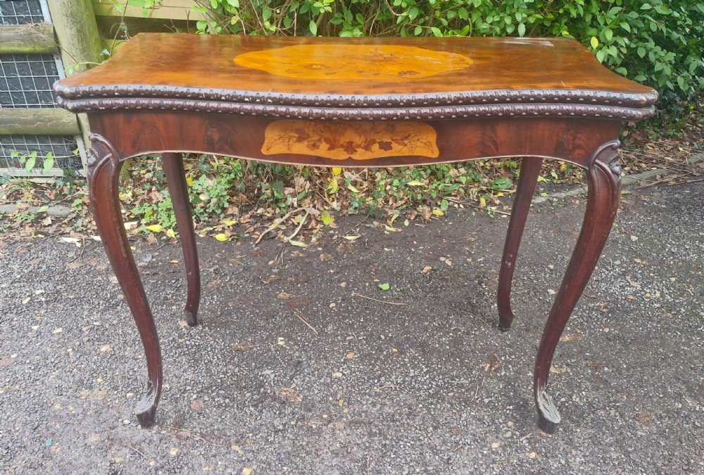 An 18th-century mahogany games table featuring a serpentine front, cabriole legs with carved knees, and marquetry inlay on the top. View XVIII