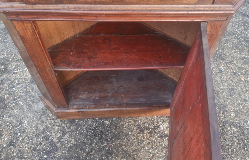 An early 18th-century floor-standing wooden corner cupboard featuring an upper door with an arched raised panel, a lower panelled door, and brass H-hinges. View II