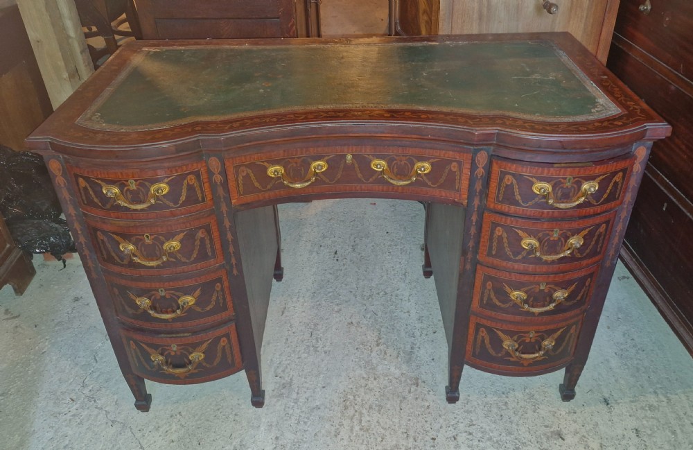A late Victorian inlaid mahogany kneehole writing desk featuring a green leather insert, multiple drawers with brass handles, and detailed floral marquetry.