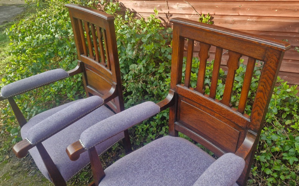 A pair of Edwardian dark oak Arts and Crafts armchairs featuring vertical back splats, upholstered armrests, and purple fabric seats with metal studding. View II