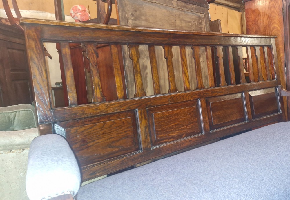 An Edwardian Arts and Crafts dark oak hall bench featuring a slatted and paneled backrest with an upholstered grey seat and padded armrests. View VII