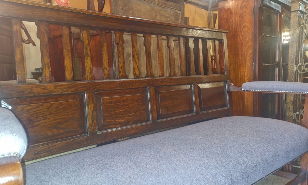 An Edwardian Arts and Crafts dark oak hall bench featuring a slatted and paneled backrest with an upholstered grey seat and padded armrests. View VIII