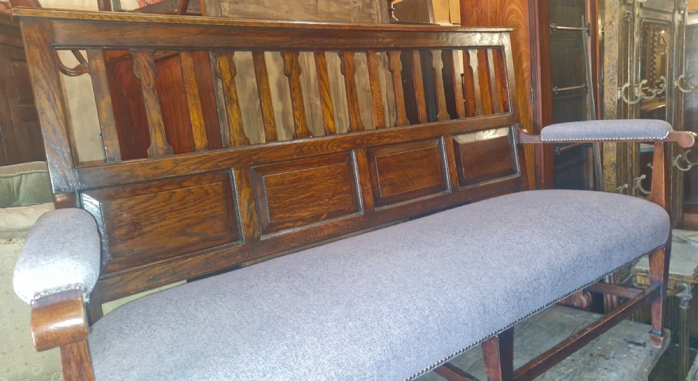 An Edwardian Arts and Crafts dark oak hall bench featuring a slatted and paneled backrest with an upholstered grey seat and padded armrests. View XIV