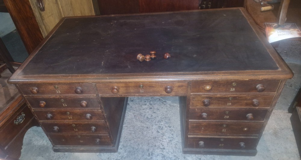 A nineteenth-century dark wood pedestal desk featuring a leather writing surface, turned wooden knobs, and numbered drawer fronts.