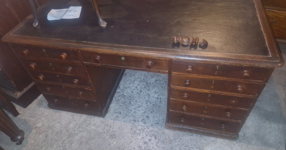 A nineteenth-century dark wood pedestal desk featuring a leather writing surface, turned wooden knobs, and numbered drawer fronts. View X