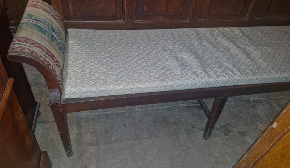 An antique dark oak settle featuring a four-panel backboard, upholstered seat cushion, patterned armrests, and square legs. View X