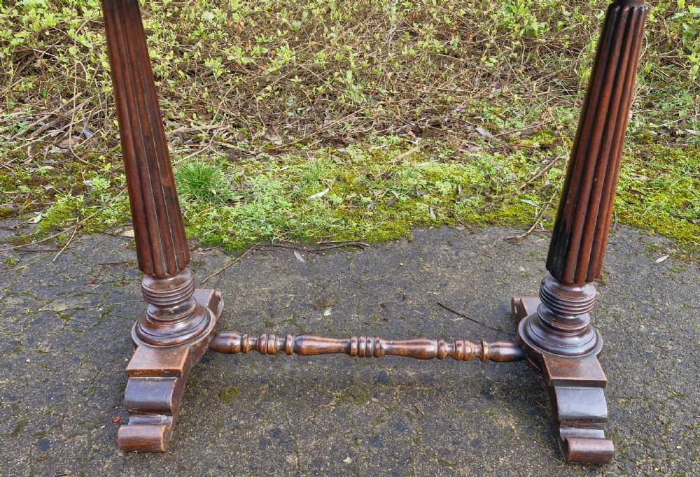 A Victorian mahogany side table featuring a tan leather insert top, scalloped apron, drop finials, and twin fluted column supports joined by a turned stretcher. View V
