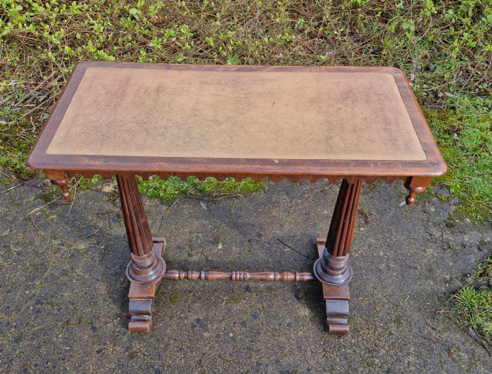 A Victorian mahogany side table featuring a tan leather insert top, scalloped apron, drop finials, and twin fluted column supports joined by a turned stretcher. View VI