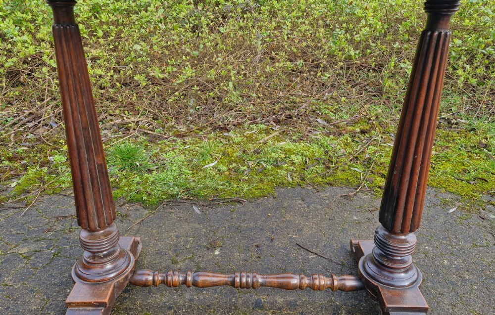 A Victorian mahogany side table featuring a tan leather insert top, scalloped apron, drop finials, and twin fluted column supports joined by a turned stretcher. View VII