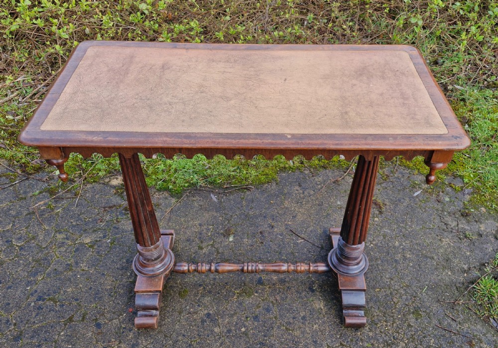 A Victorian mahogany side table featuring a tan leather insert top, scalloped apron, drop finials, and twin fluted column supports joined by a turned stretcher. View VIII