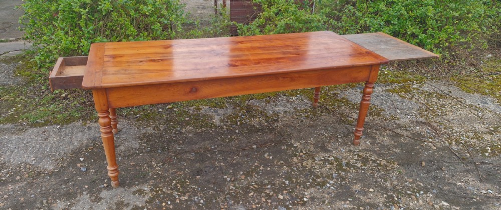 A long rectangular wooden French farmhouse dining table featuring turned legs, an open side drawer, and an extended pull-out bread slide. View VIII