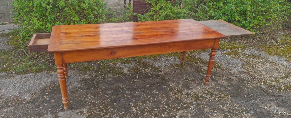 A long rectangular wooden French farmhouse dining table featuring turned legs, an open side drawer, and an extended pull-out bread slide. View XII