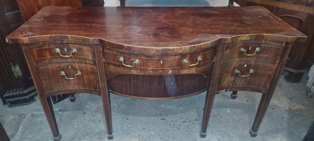 A Late Georgian mahogany serpentine front sideboard featuring line inlay, brass handles, and tapered square legs.