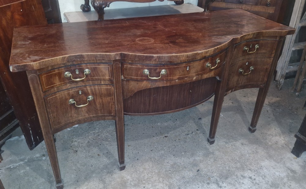 A Late Georgian mahogany serpentine front sideboard featuring line inlay, brass handles, and tapered square legs. View VI