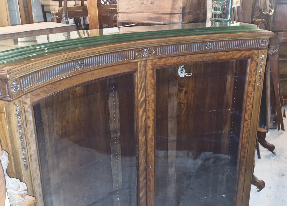 An Edwardian mahogany concave bookcase featuring twin glazed doors, fluted frieze moulding, and carved floral detailing. View III