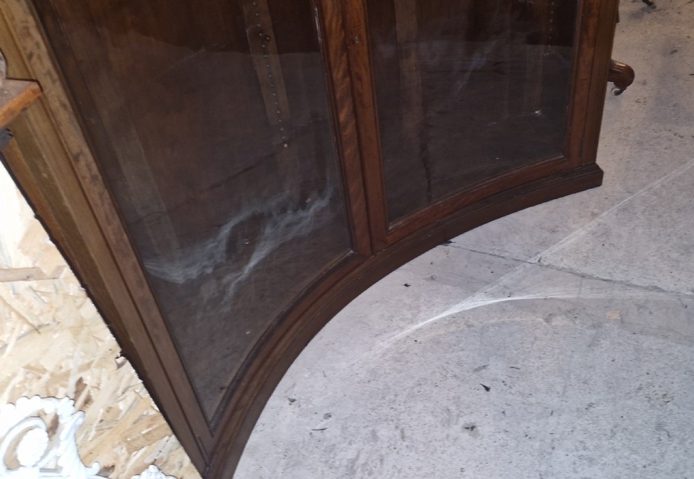 An Edwardian mahogany concave bookcase featuring twin glazed doors, fluted frieze moulding, and carved floral detailing. View V