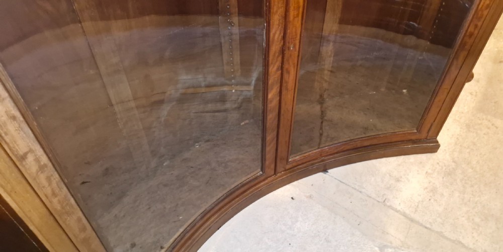 An Edwardian mahogany concave bookcase featuring twin glazed doors, fluted frieze moulding, and carved floral detailing. View IX