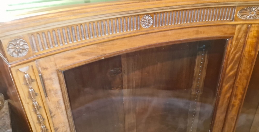 An Edwardian mahogany concave bookcase featuring twin glazed doors, fluted frieze moulding, and carved floral detailing. View X