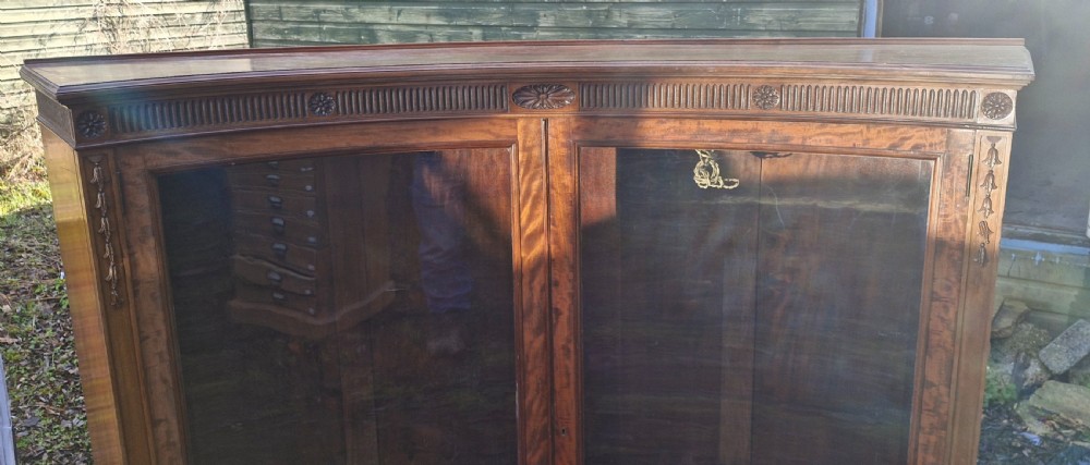 An Edwardian mahogany concave bookcase featuring twin glazed doors, fluted frieze moulding, and carved floral detailing. View XII
