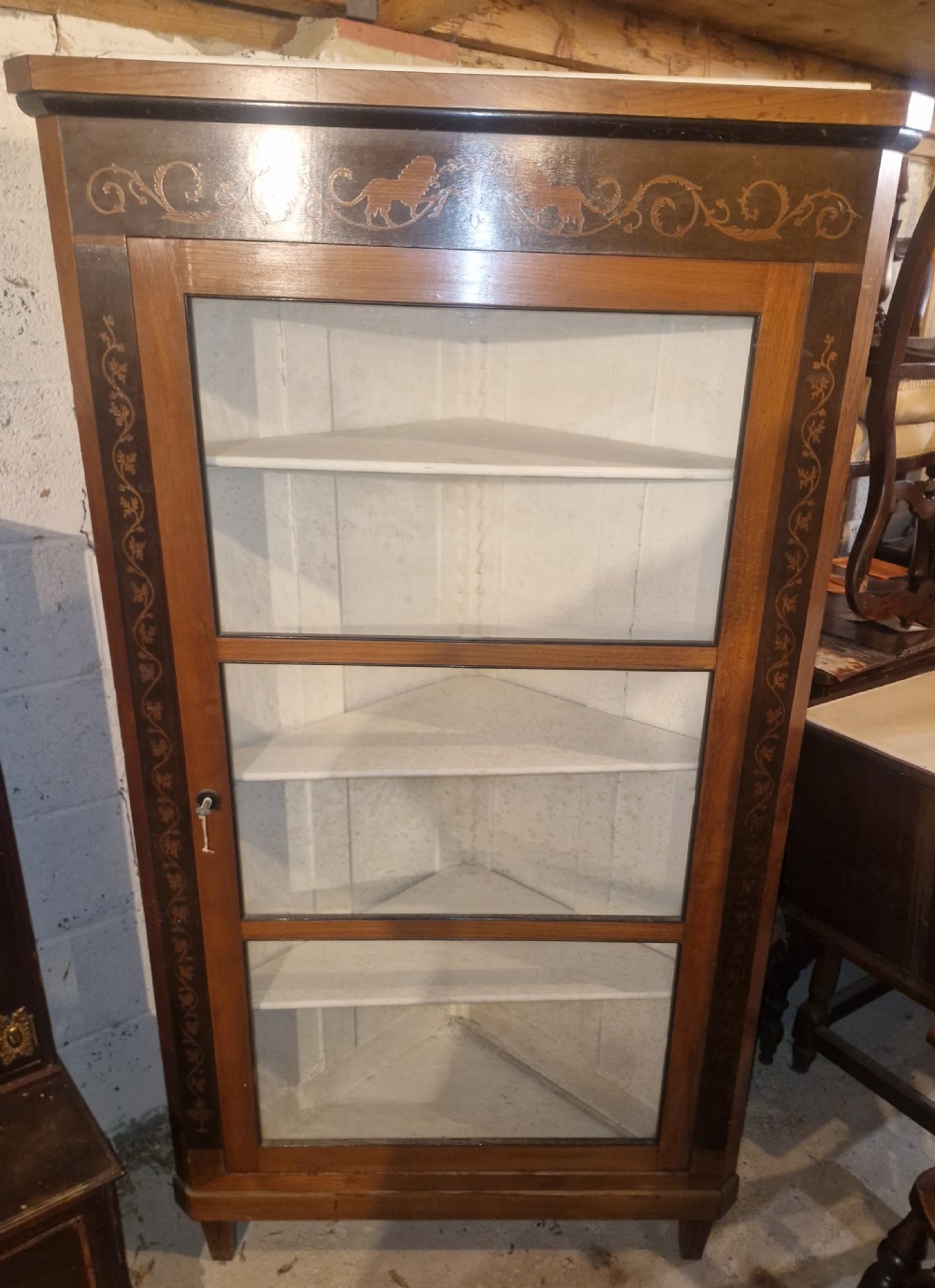A tall Danish wooden corner cabinet featuring a glazed front door, decorative inlaid scrolling borders, and internal shelves painted off-white. View VII
