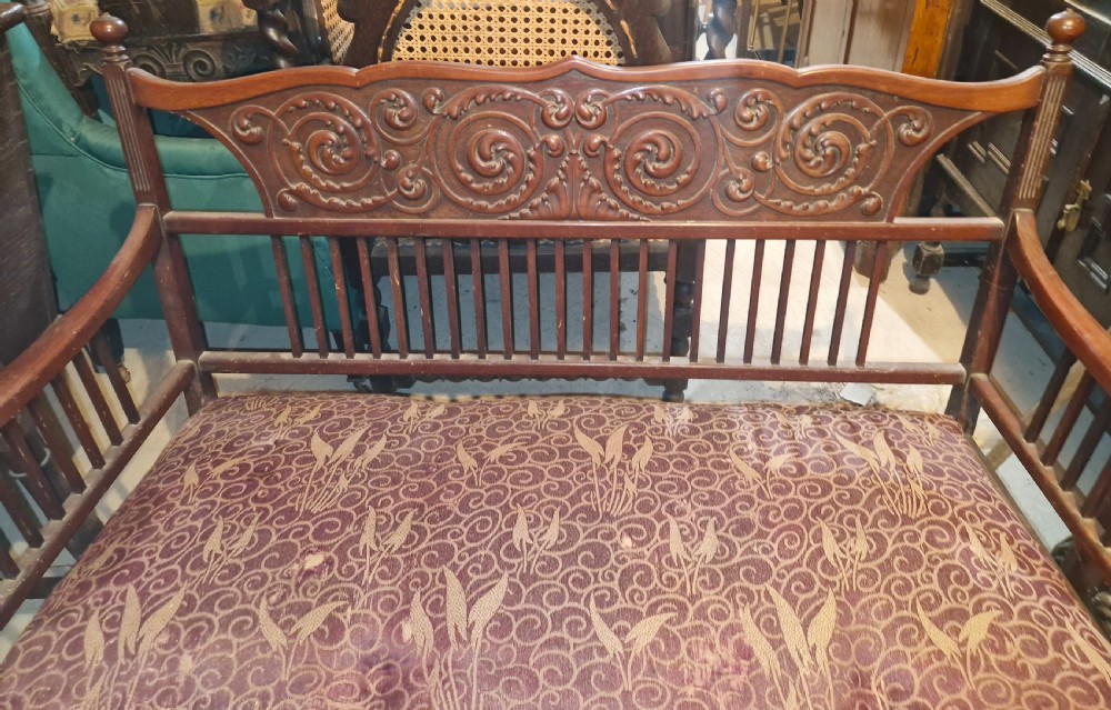 A late Victorian mahogany settee with carved scroll detailing across the top rail, spindle backrest, curved arms, and a patterned red fabric seat on legs with brass castors. View III