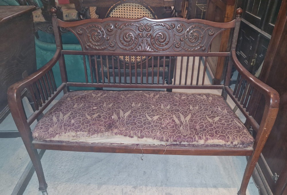 A late Victorian mahogany settee with carved scroll detailing across the top rail, spindle backrest, curved arms, and a patterned red fabric seat on legs with brass castors. View VII