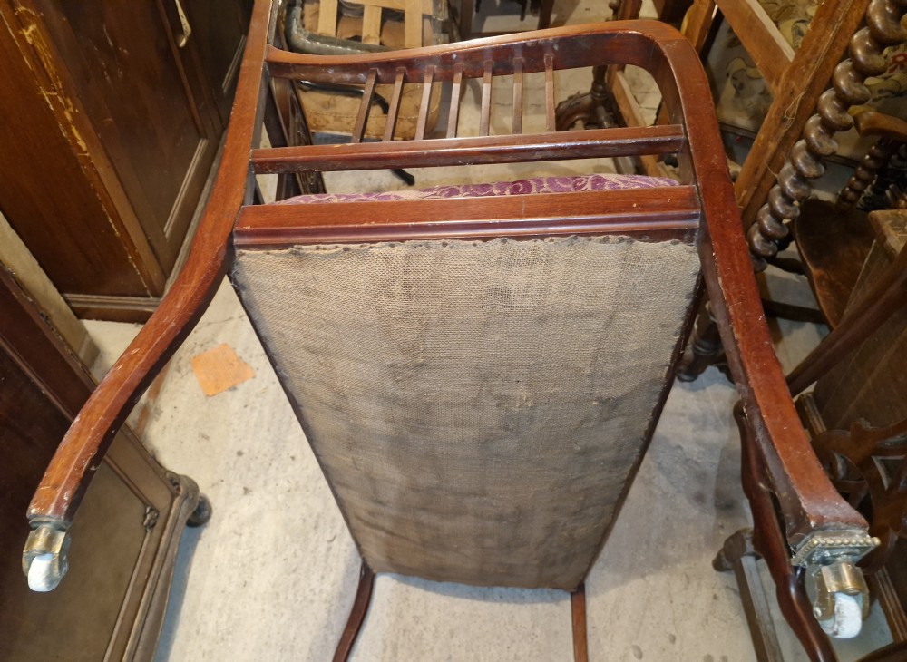A late Victorian mahogany settee with carved scroll detailing across the top rail, spindle backrest, curved arms, and a patterned red fabric seat on legs with brass castors. View IX